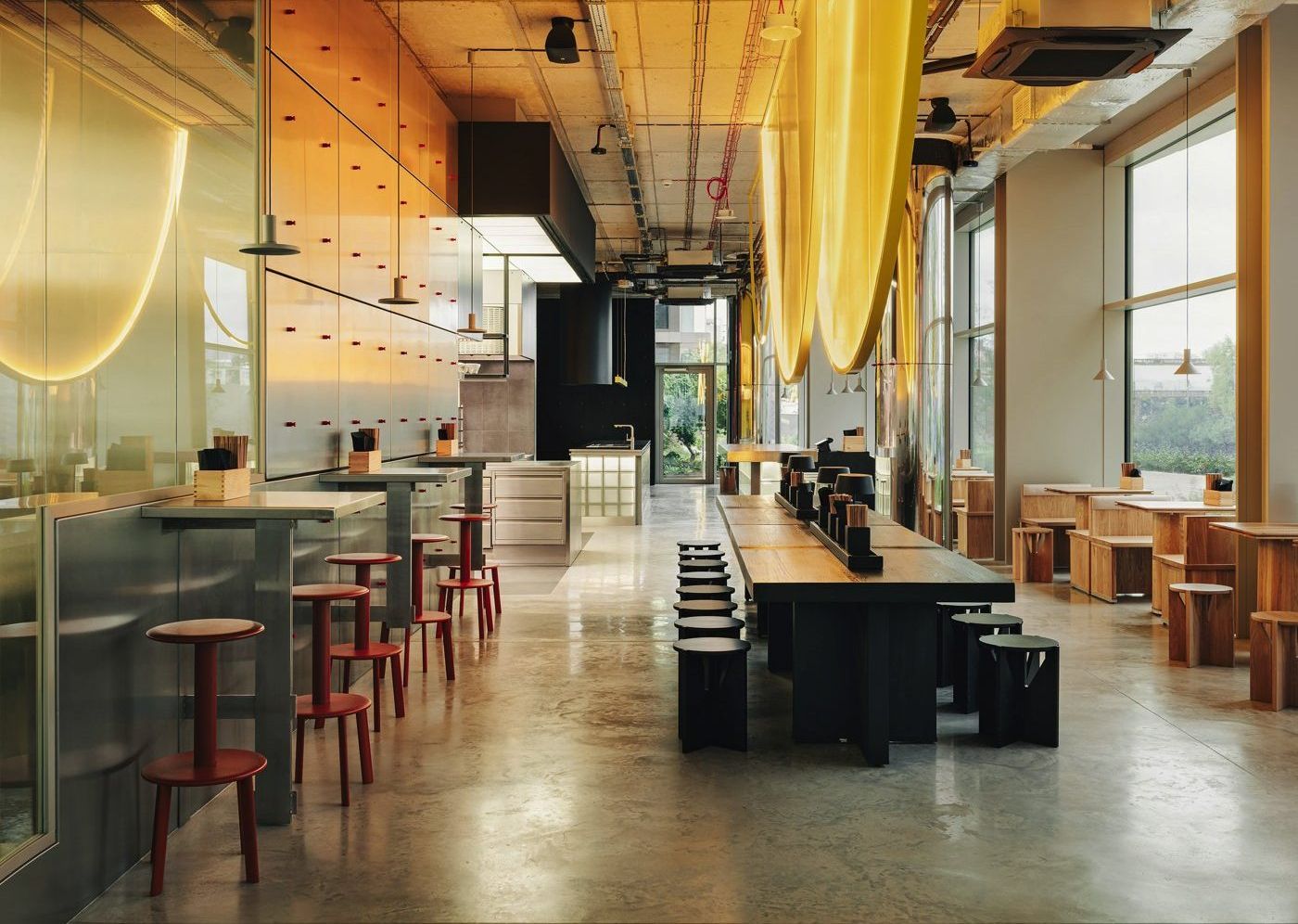 ato ramen (Warszawa) — 긴 홀 — 왼쪽 스테인리스 벽 스탠딩석, 가운데 검은 공용 테이블, 오른쪽 창가 원목석