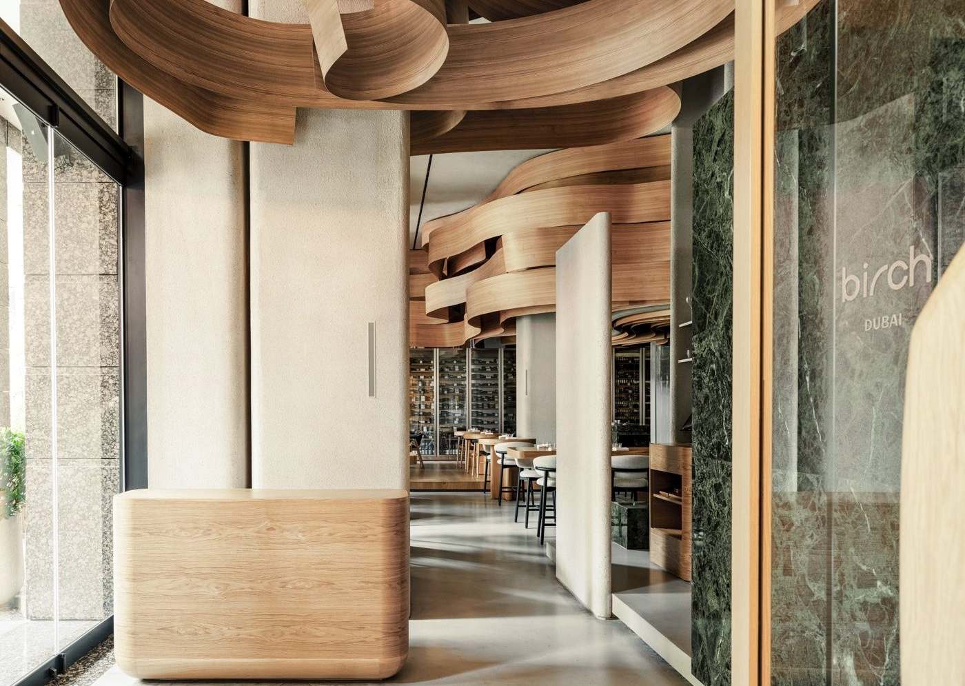 Birch restaurant (Dubai) — 입구. 곡면 원목 카운터와 짙은 초록 대리석 벽