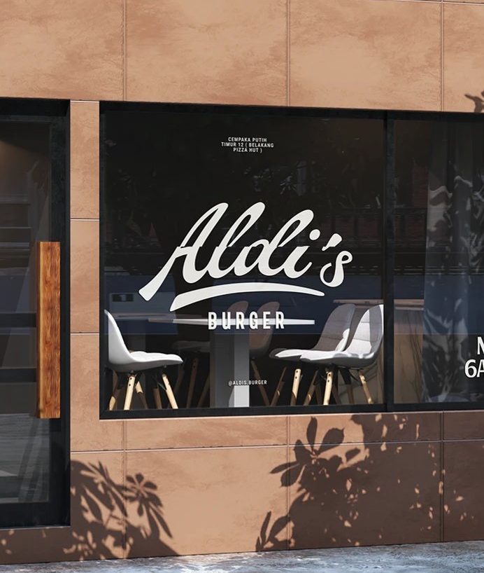 Aldi's Burger Visual Identity — 매장 유리창. 흰 필기체 Aldi's 와 BURGER, 안쪽 의자가 비친다