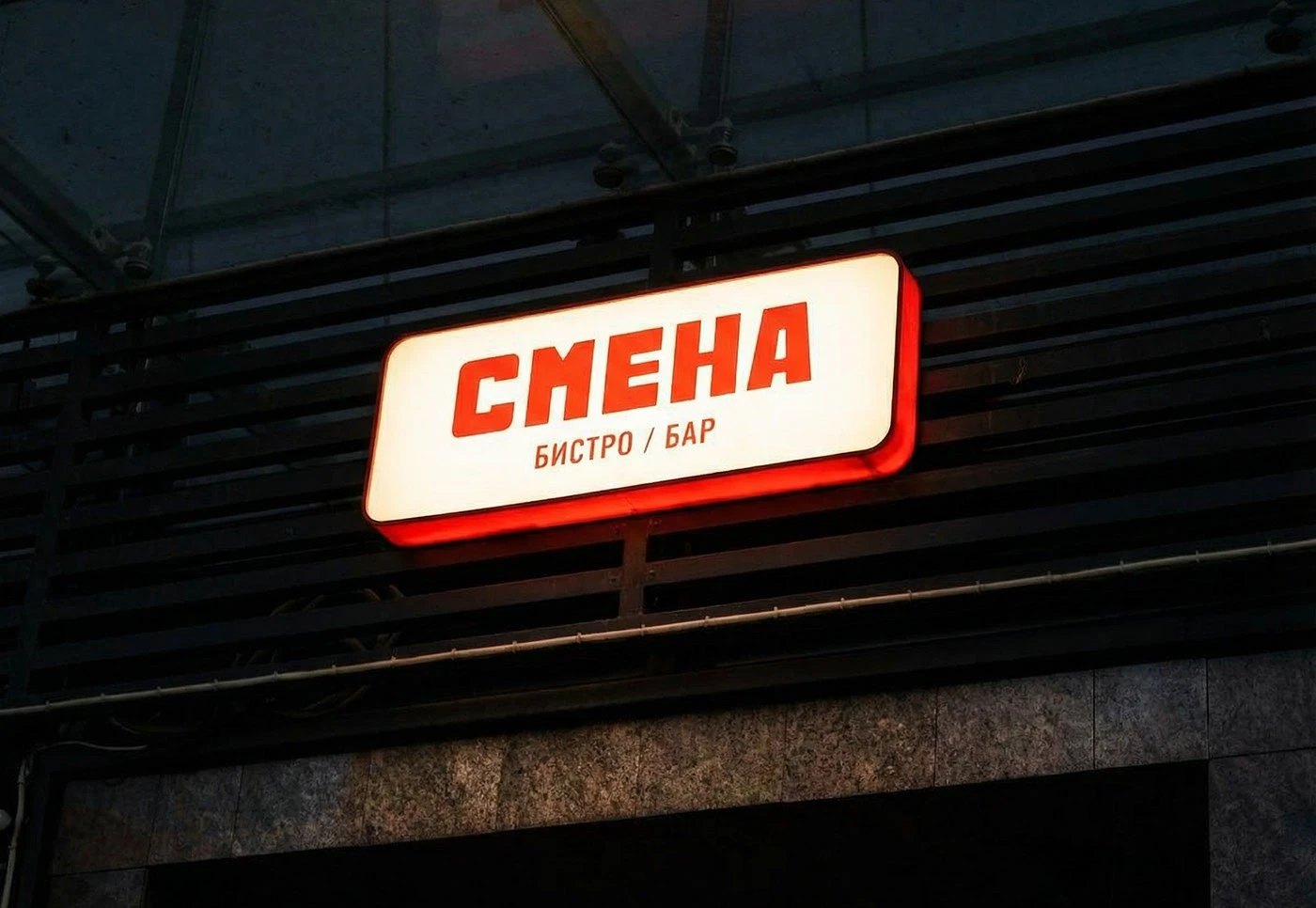 СМЕНА bistro / bar — 밤의 간판. 어두운 정면에 빛나는 상자 간판 하나, 빨간 로고