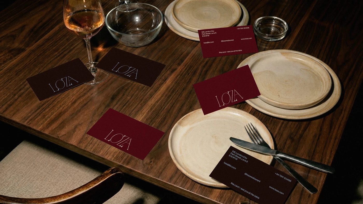loza / restaurant — 나무 식탁 위 명함. 와인색과 흙색 두 가지