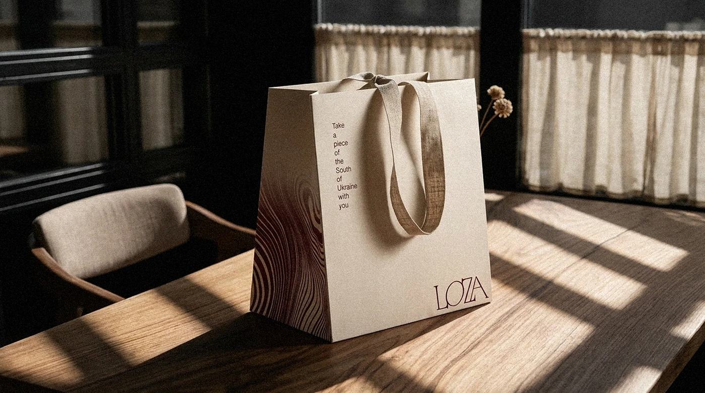 loza / restaurant — 크림색 종이 가방. 나뭇결 같은 가는 선 무늬와 작은 로고