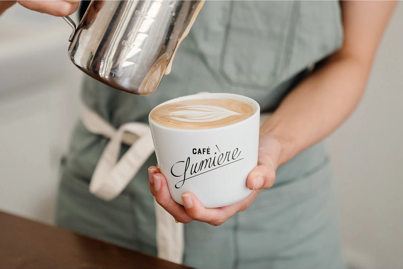 Café Lumière — 라테아트를 붓는 바리스타. 도자기 컵의 로고